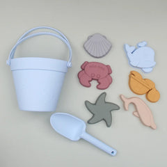 Set of beach toys including a bucket, shovel, and sea creature molds on a beige background