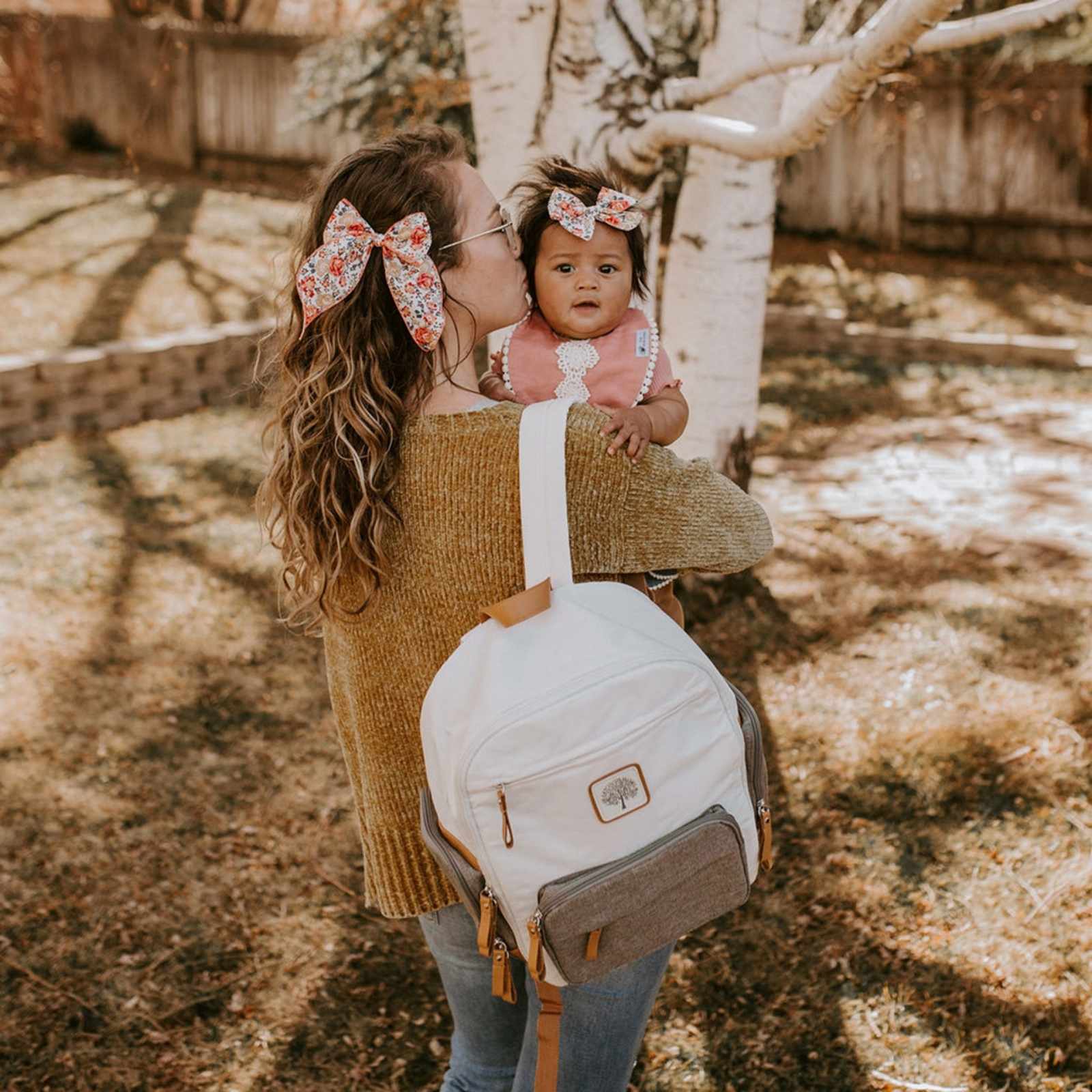 Woman holding a baby with a white backpack outdoors