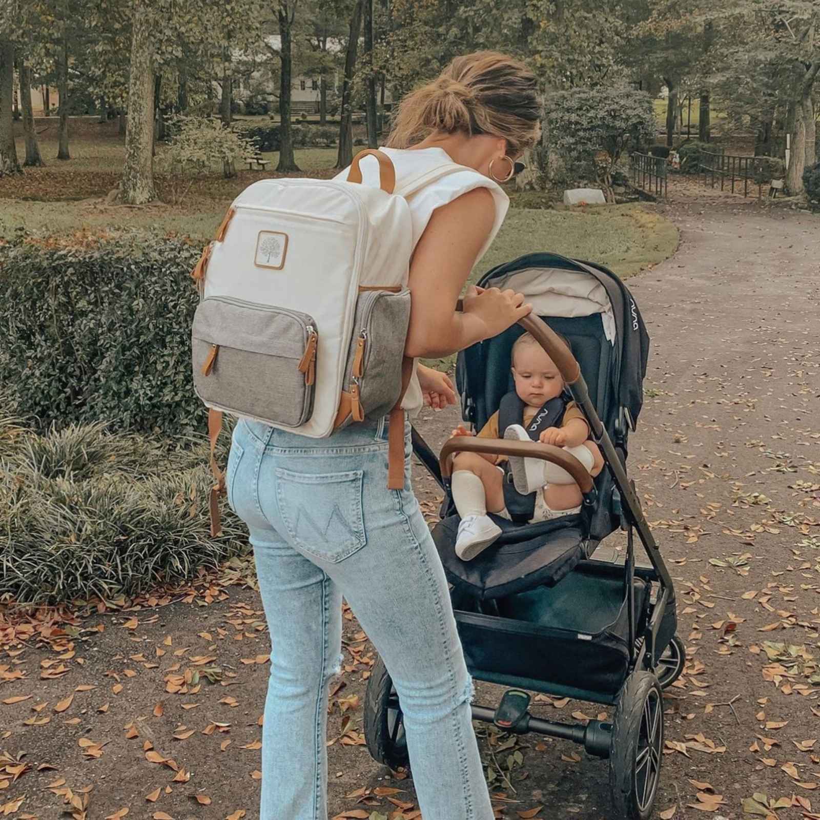 Woman with a backpack and baby in a stroller in a park