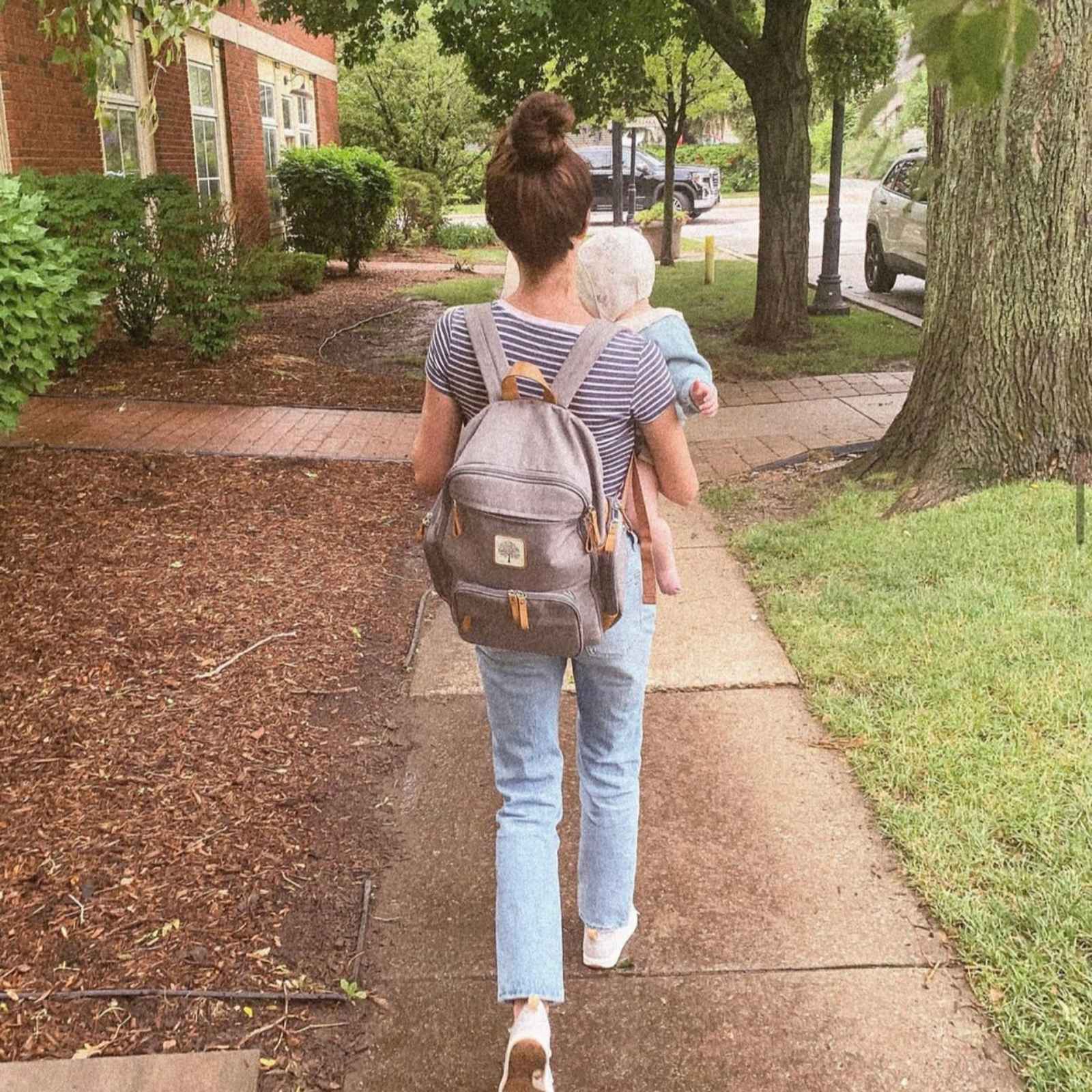 Woman walking with a backpack and an elderly person on a sidewalk.