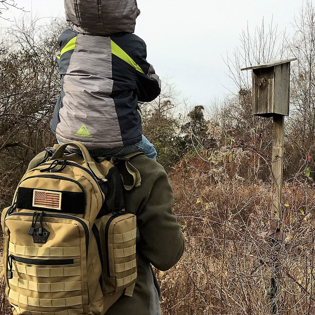 Person with a child on their shoulders wearing a large backpack in a natural setting.