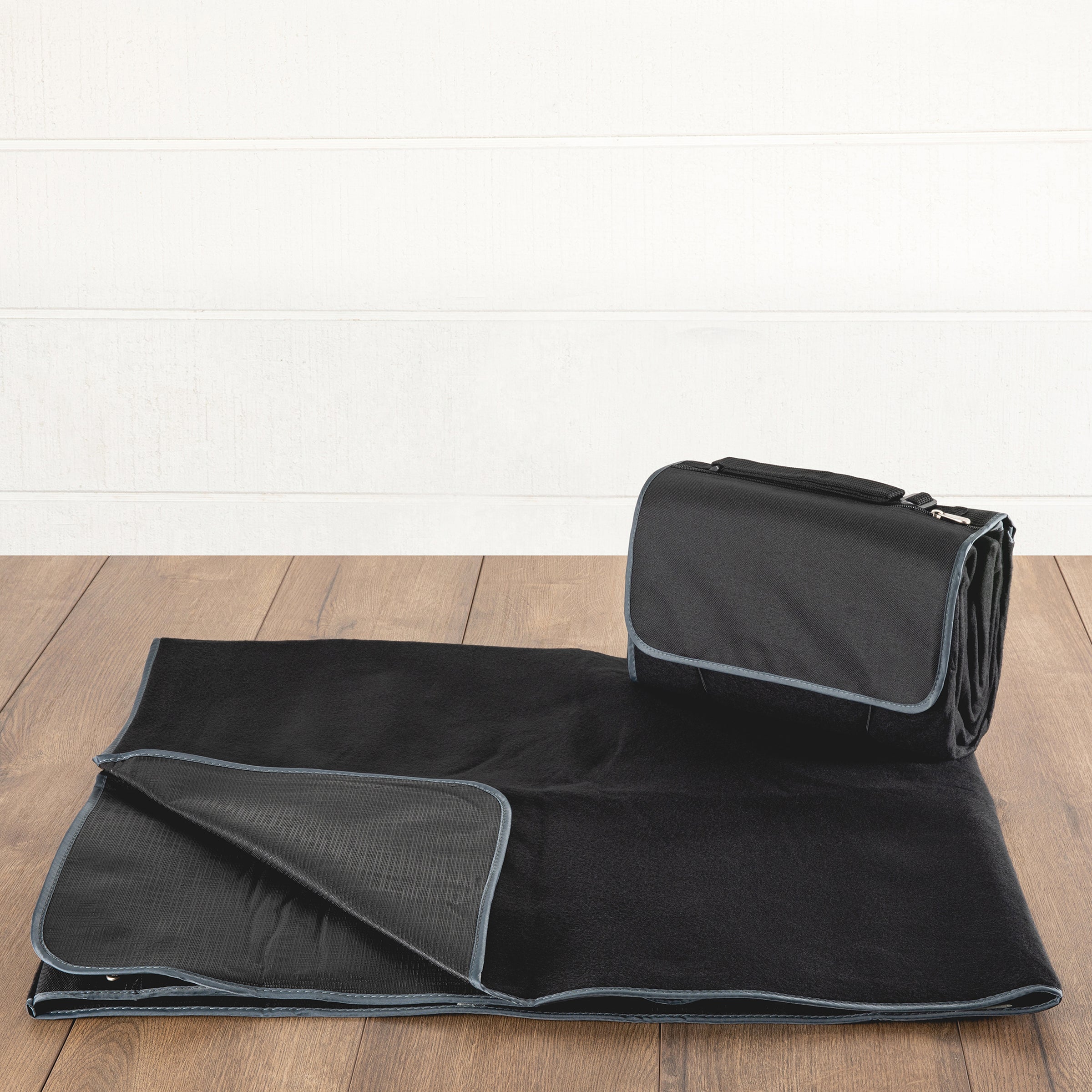 Black picnic blanket with a carrying handle on a wooden floor.