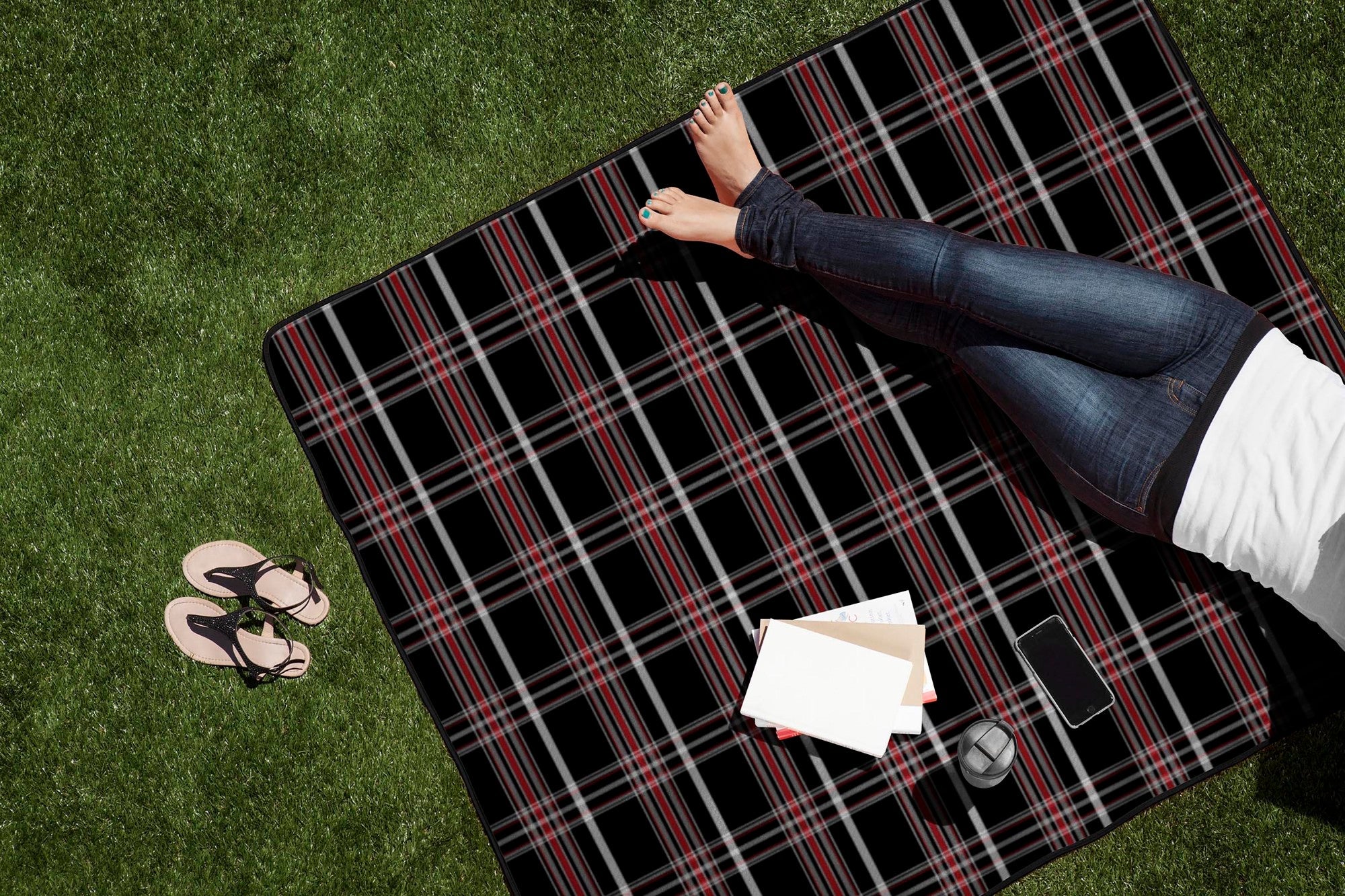 Person lying on a black and red plaid picnic blanket on grass