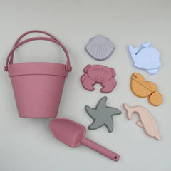 Pink sand pail and shovel with beach-themed molds on a light gray background