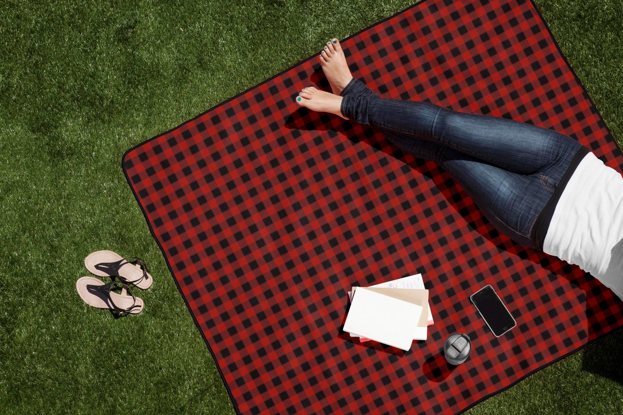 Person sitting on a red and black checkered picnic blanket on grass