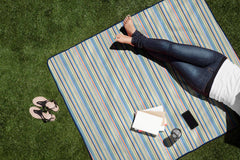 Person lying on a striped picnic blanket with a tablet and phone on a grassy area
