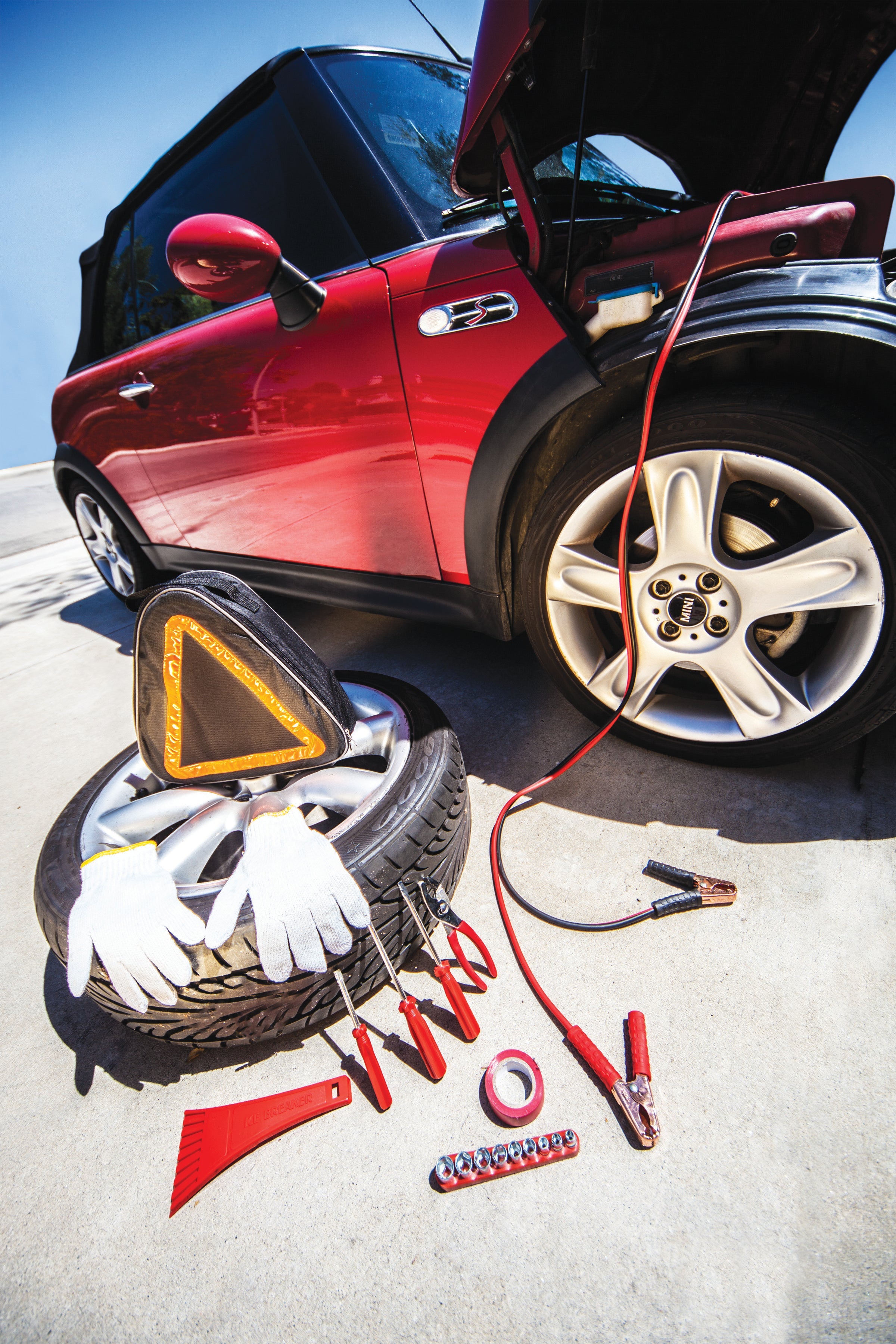 Red car with open hood, tire, jack, and tools on a road