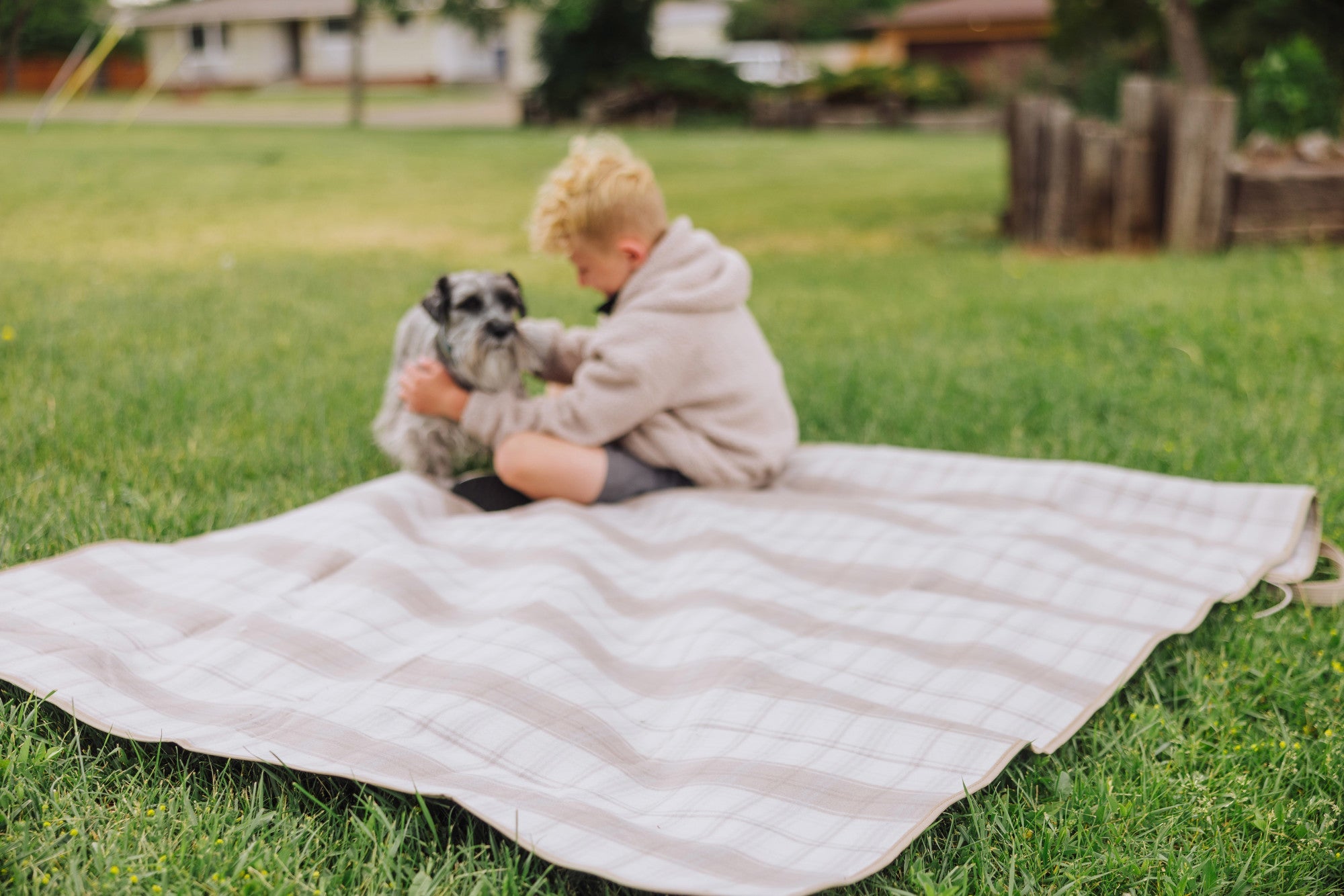 Child sitting on a quilt with a dog in a grassy area