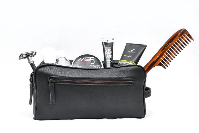 Black leather toiletry bag with grooming products and a comb on a white background
