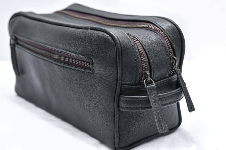 Black leather toiletry bag with multiple zippers on a white background