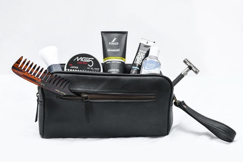 Black toiletry bag with grooming products including a comb, bottles, and a razor on a white background