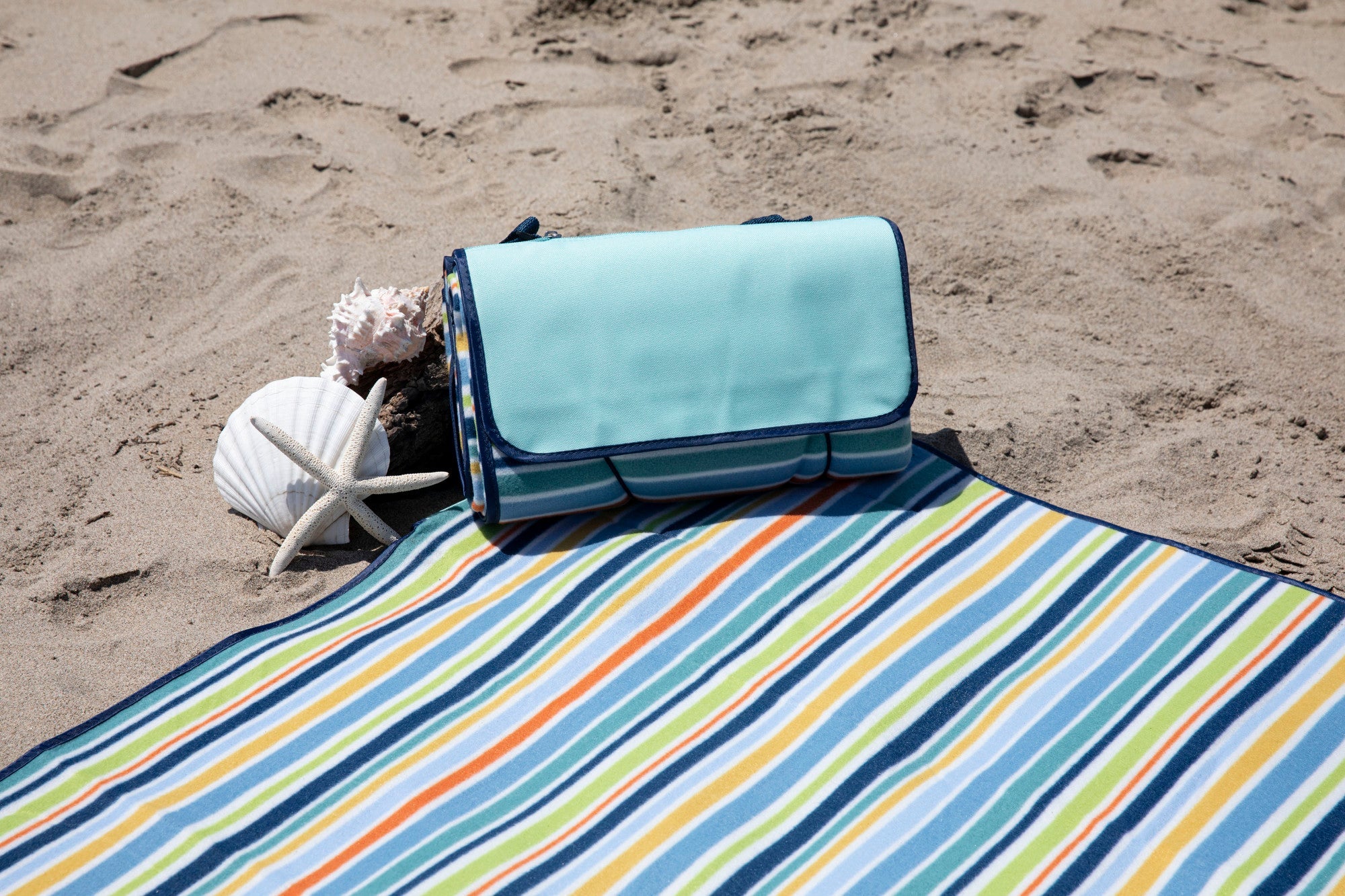 Colorful striped beach mat with a turquoise roll-up bag on sandy beach
