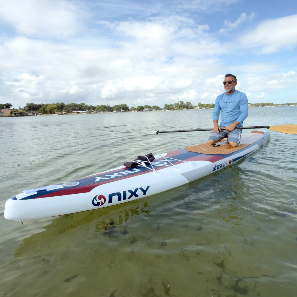 Man on a Nixy paddleboard on a calm body of water with a clear sky.