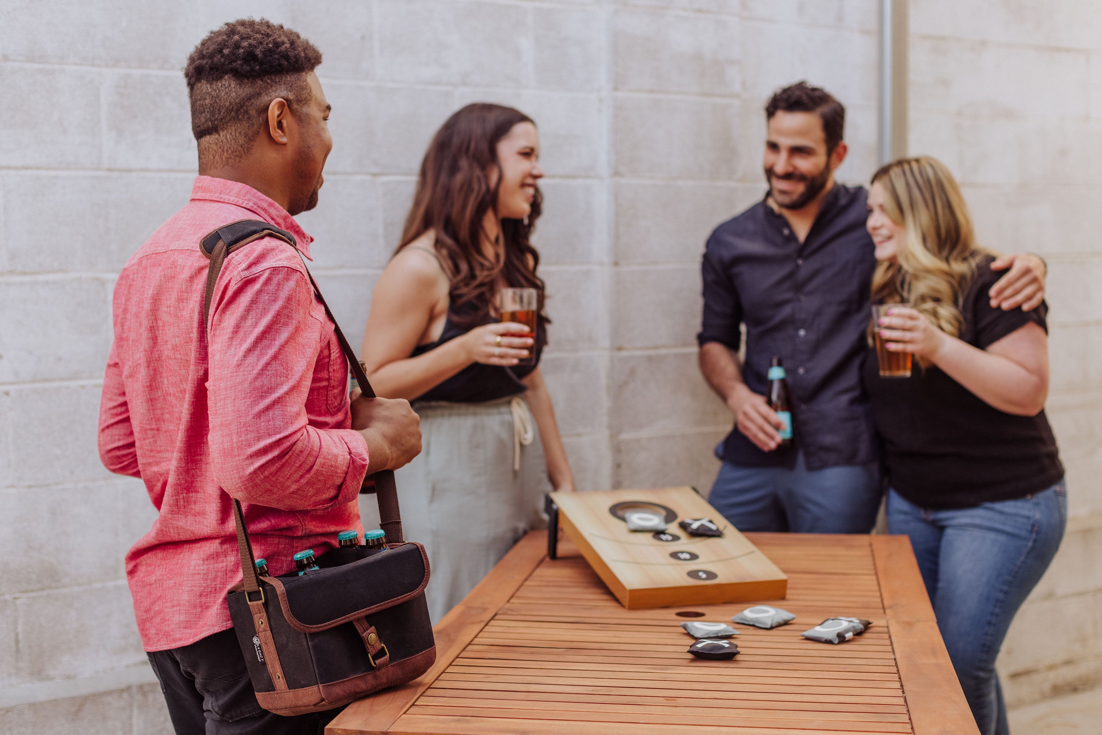 Four friends socializing around a wooden table with drinks and a guitar case.