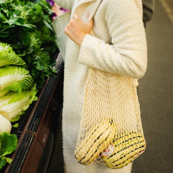 Person holding a mesh bag with groceries in a supermarket setting