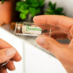 Person holding a small glass container labeled 'Bamboo Switch' with greenery in the background.