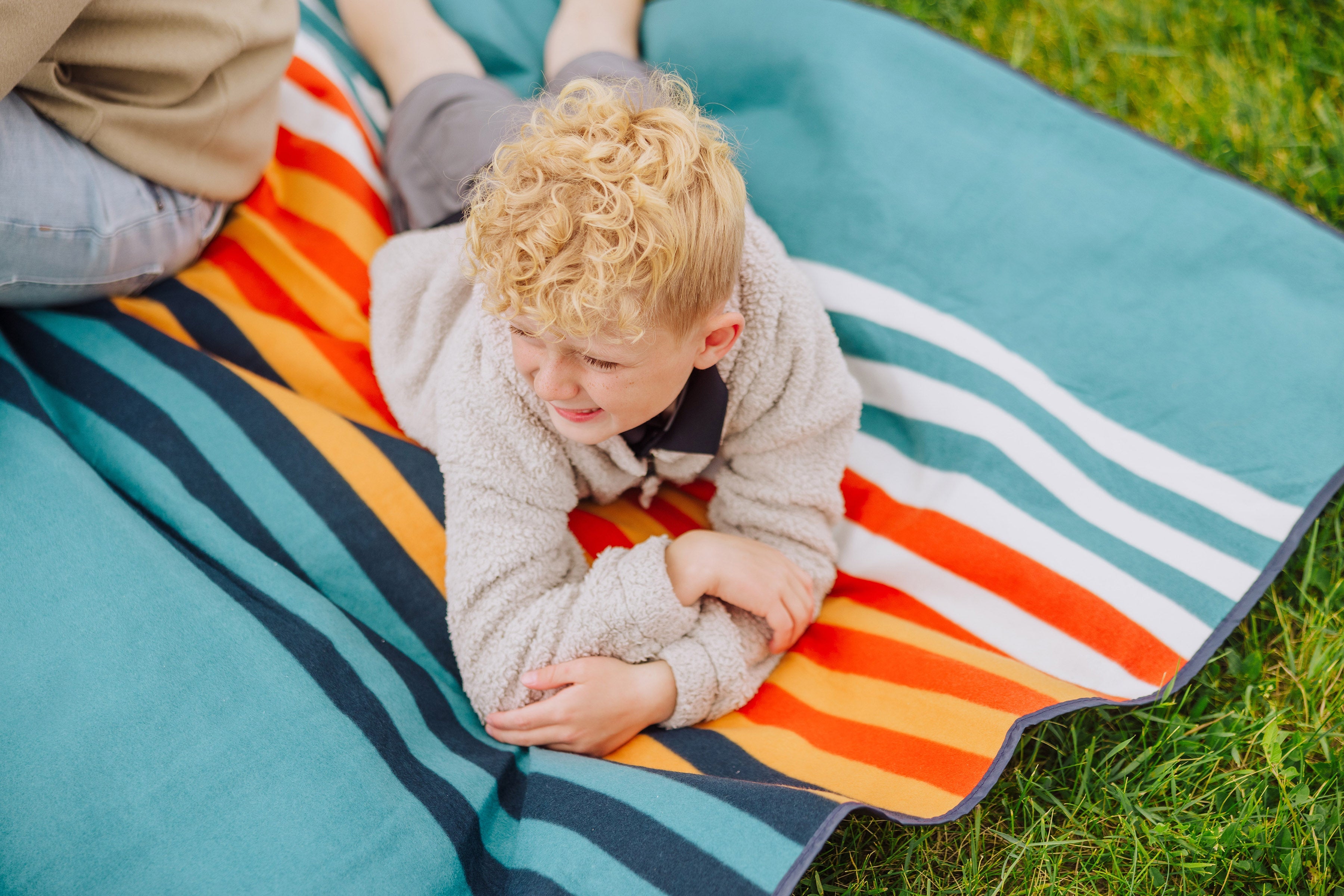 Child lying on a colorful striped blanket in a grassy area