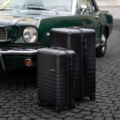 Two black suitcases on a cobblestone street with a classic green car in the background.