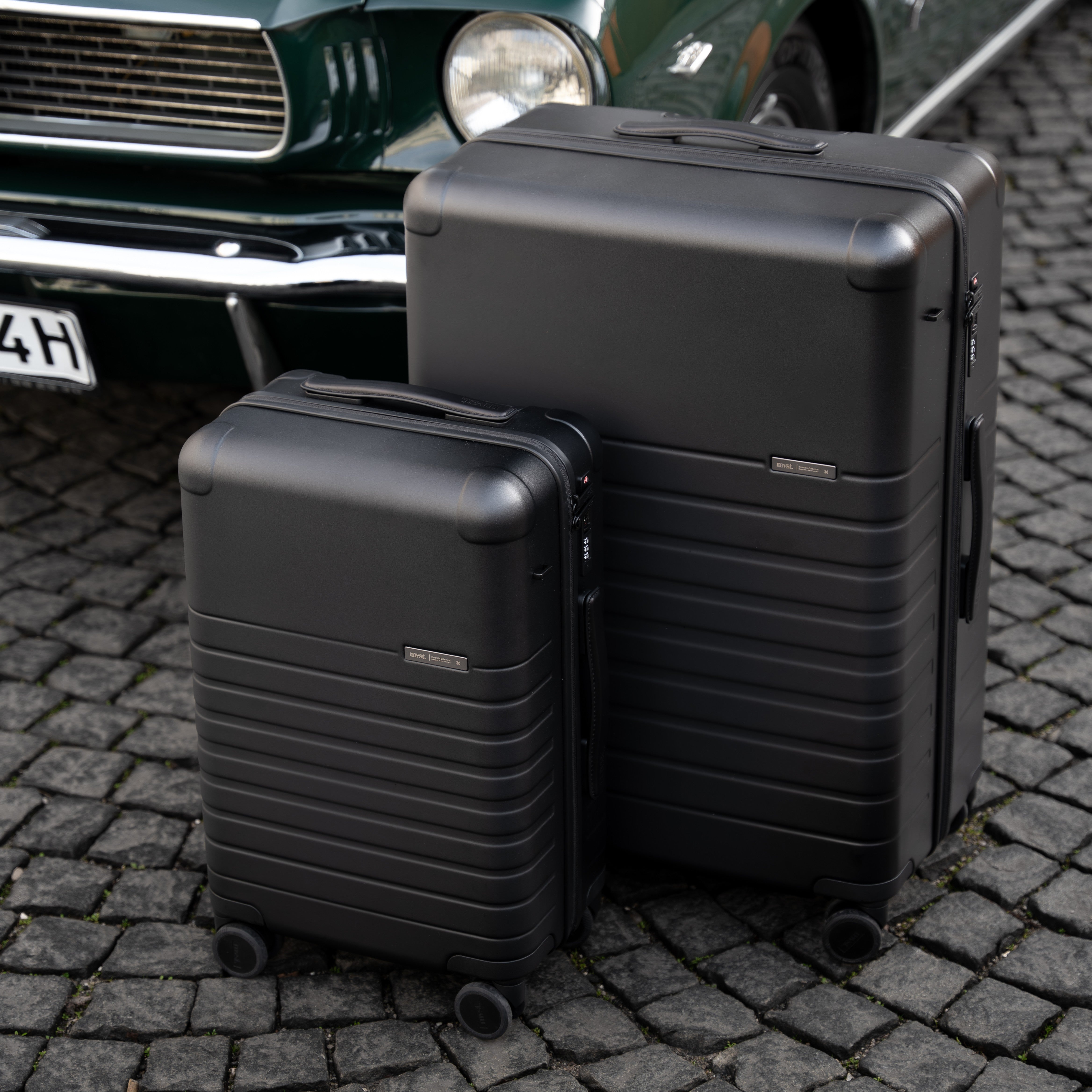 Two black suitcases on a cobblestone street with a car in the background.