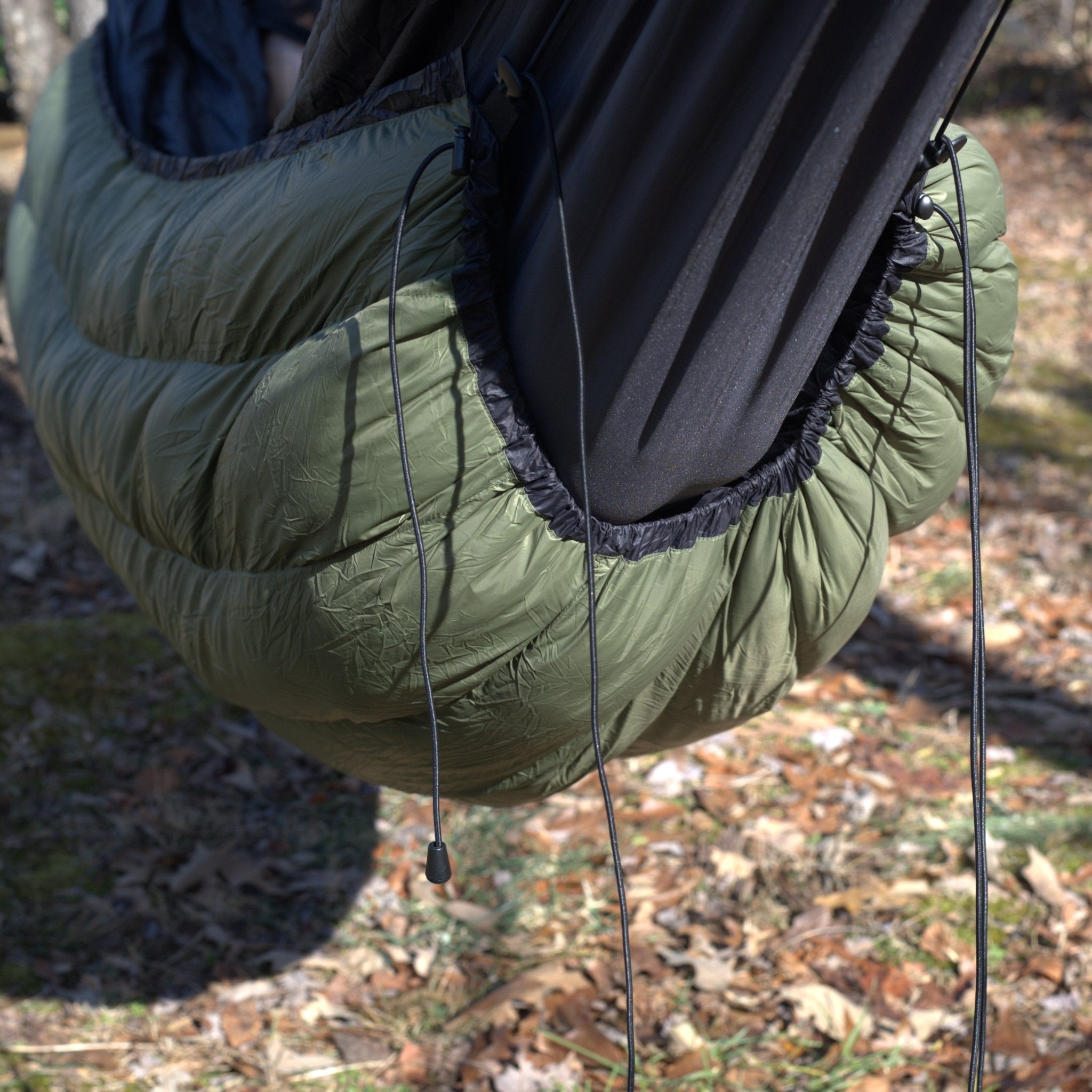 Green sleeping bag with black trim hanging outdoors on a blurred natural background