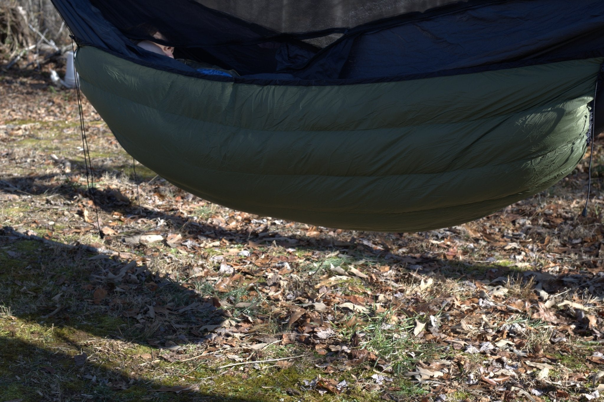 Green sleeping bag hanging from a hammock in a natural setting