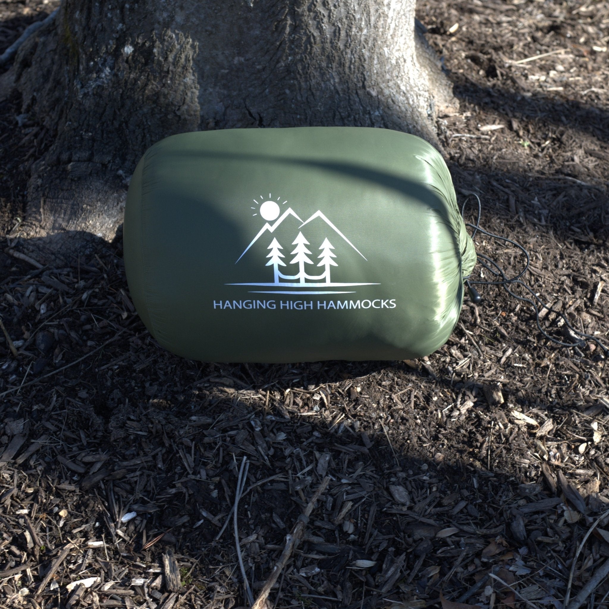 Green hammock bag with 'Hanging High Hammocks' logo on a forest floor background