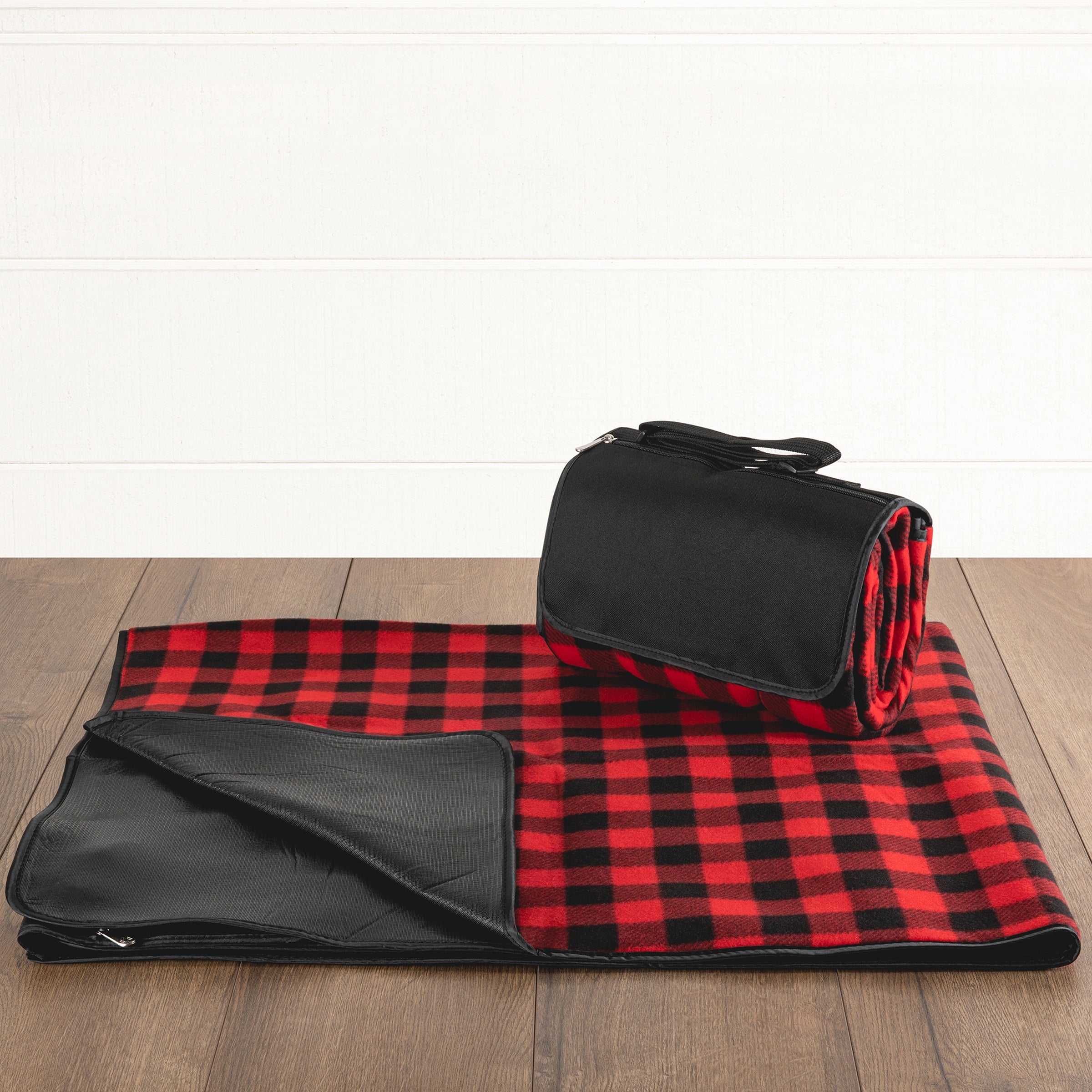 Red and black checkered picnic blanket with a black carrying bag on a wooden floor.