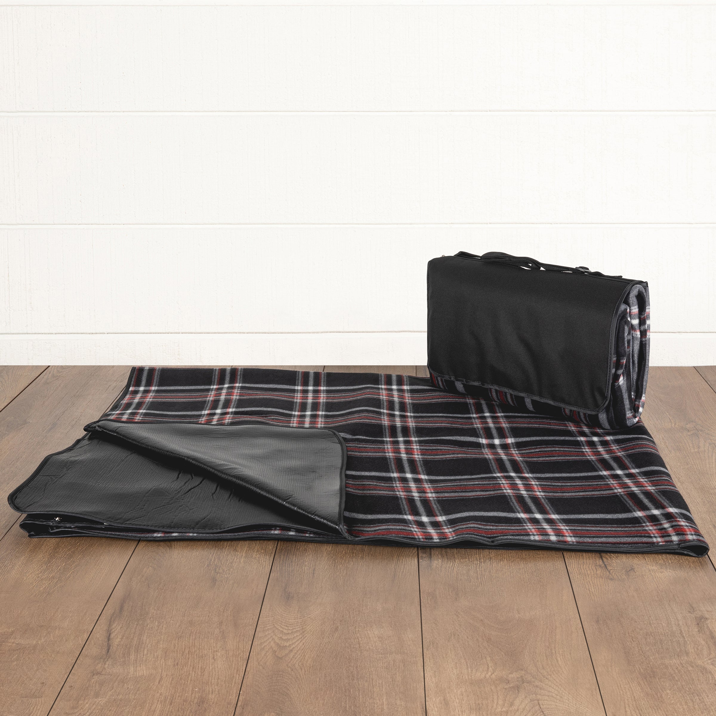 Plaid blanket with black border and storage bag on a wooden floor.
