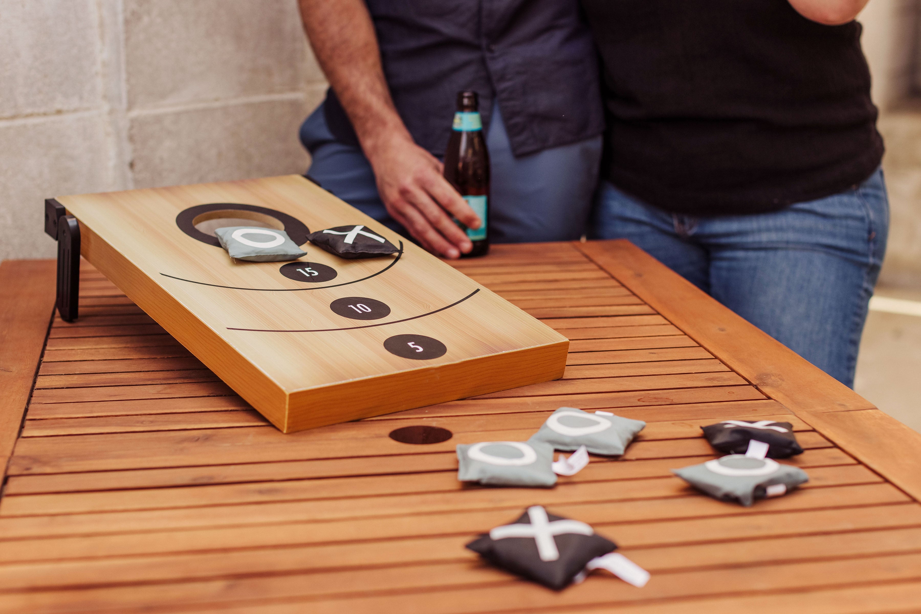 Wooden beer pong table with cups on a wooden surface, with a person in the background.
